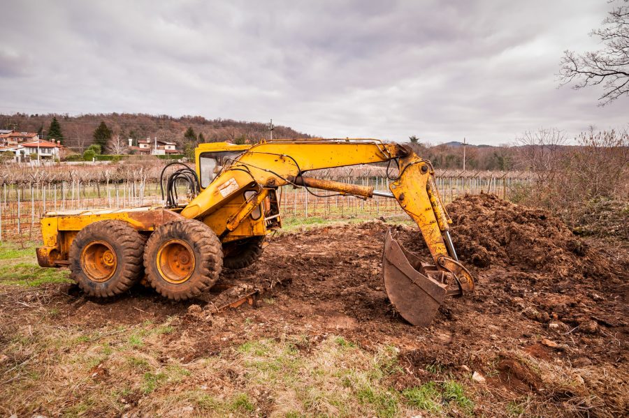 Yellow excavator digging soil in rural landscape